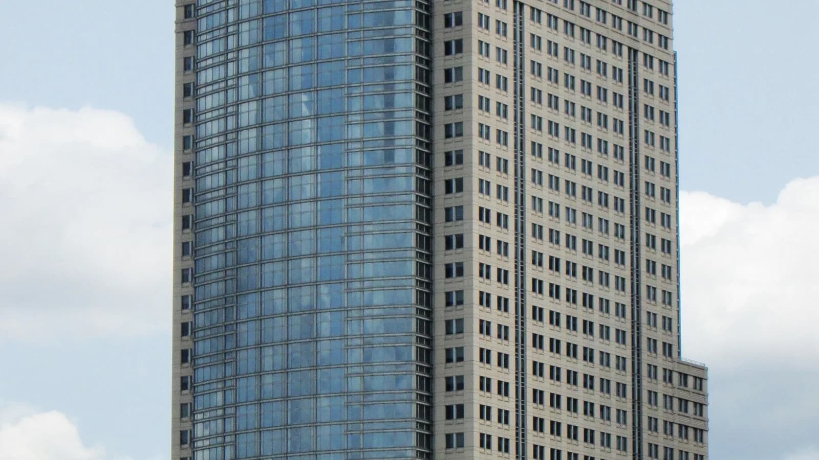 Hochhaus 388 Greenwich Street in Manhattan mit Glas- und Steinfassade und Uhr am Dachaufbau, gesehen vom Hudson River, davor Uferpromenade und Segelboote unter leicht bewölktem Himmel