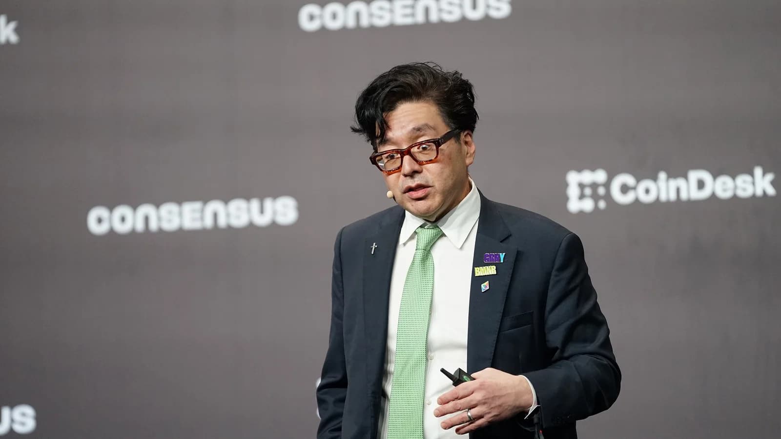 Tom Lee spricht in dunklem Anzug und grüner Krawatte mit Headset auf der Bühne von Consensus Hong Kong 2026, im Hintergrund Logos von Consensus und CoinDesk