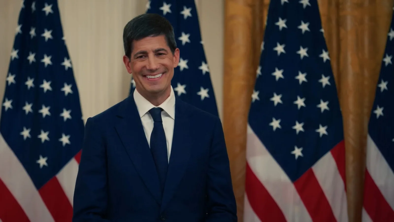 Kevin Warsh, Vorsitzender der US-Notenbank Fed, lächelnd im dunkelblauen Anzug vor US-Flaggen und goldenem Vorhang im Weißen Haus